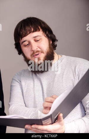 Büroangestellter zeigt Bericht aus seinen Händen auf mit grauem Hintergrund. Stockfoto