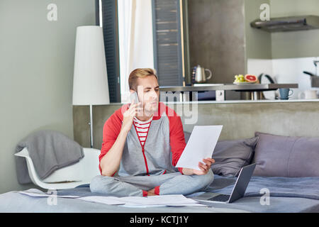 Moderner Mitarbeiter, der zu Hause Papiere liest und auf dem Smartphone spricht Stockfoto