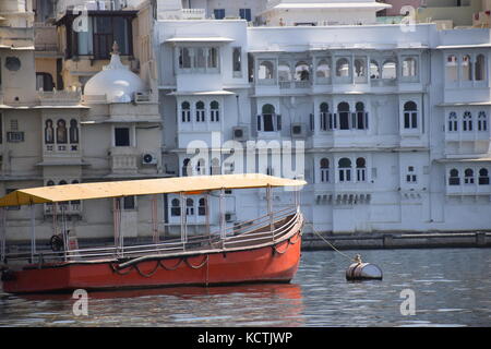 Gebäude und eine orangefarbene Boot entlang des Lake Pichola in Udaipur, Rajasthan - Indien Stockfoto