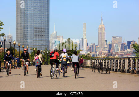 Besucher, die im Liberty State Park mit Goldman Sachs Tower und Midtown Manhattan Skyline und Empire State Building im Hintergrund radeln.New Jersey.USA Stockfoto