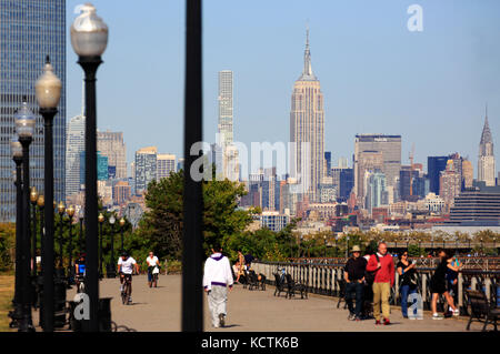 Besucher am Hudson River Waterfront Walkway im Liberty State Park mit der Skyline von Midtown Manhattan NYC und dem Empire State Building im Hintergrund.NJ.USA Stockfoto