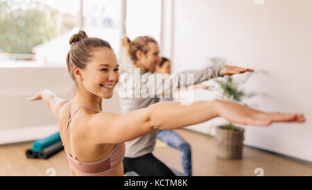 Lächelnd sportliche Frau tun Krieger posieren in Yoga class. Glückliche junge Frauen Yoga im Fitnessstudio Klasse. Stockfoto