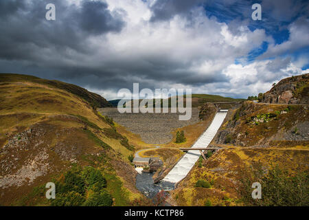 Regenwolken über dem Felsen gefüllt Llyn brianne Damm, Anzeigen der Abflußkanal entfernt auf der rechten Seite. Stockfoto