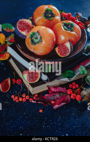 Reife persimonen auf einem Stapel Bücher in einem dunklen Herbst Stillleben mit Früchten und Beeren. Ernte Konzept. dunklen Essen Fotografie mit kopieren. Stockfoto