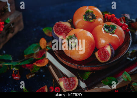 Reife persimonen auf einem Stapel Bücher in einem dunklen Herbst Stillleben mit Früchten und Beeren. Ernte Konzept. dunklen Essen Fotografie mit kopieren. Stockfoto