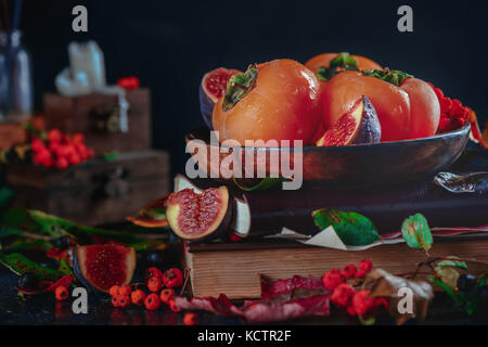 Reife persimonen auf einem Stapel Bücher in einem dunklen Herbst Stillleben mit Früchten und Beeren. Ernte Konzept. dunklen Essen Fotografie mit kopieren. Stockfoto