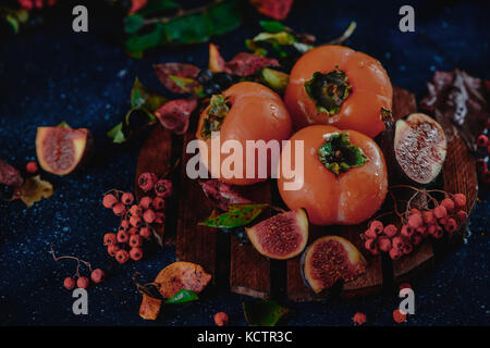 Reife persimonen auf Holzplatte in einem dunklen Herbst Stillleben mit Früchten und Beeren. Ernte Konzept. dunklen Essen Fotografie mit kopieren. Stockfoto