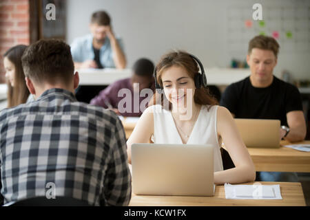 Lächelnd Geschäftsfrau in Kopfhörer Laptop Bildschirm am Arbeitsplatz in Shared Office suchen. freundlich Büroangestellter in on-line-Konferenz teilnehmen, Stockfoto