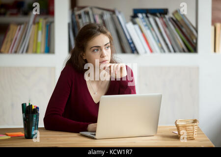 Nachdenkliche junge weibliche Unternehmer vor Laptop. casual Geschäftsfrau, denken über die Möglichkeit der Suche nach neuen Geschäftschancen. freela Stockfoto