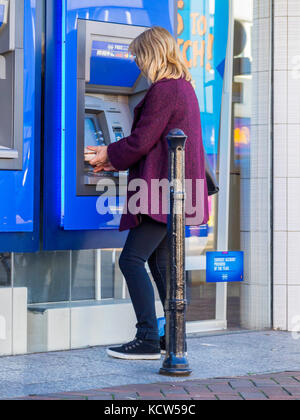 Eine junge blonde Frau Geld abheben von einem Halifax Bank ATM oder Geldautomat Stockfoto