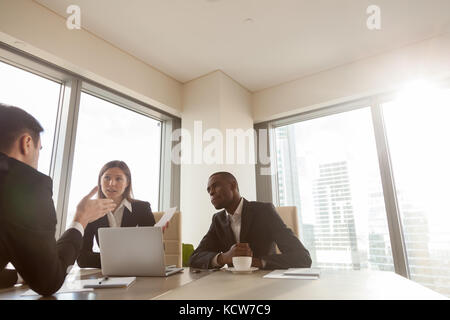 Ein afroamerikanischer Geschäftsmann hört seinen kaukasischen Geschäftspartnern während der Verhandlungen aufmerksam zu. Geschäftsfrau diskutiert Ideen und Vorschläge o Stockfoto