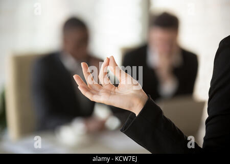 Nahaufnahme Bild der weiblichen Palm mit den Fingern im Jnana mudra Geste mit unscharfen Silhouetten von sprechen Geschäftsleute auf Hintergrund gefaltet. geschäftsfrau Stockfoto