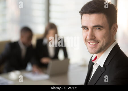 Headshot Portrait von erfolgreichen kaukasischen Geschäftsmann an Kamera suchen, Mann in Schwarz und Weiß mit Laptop im Hintergrund Frau. lächelnd Leader Stockfoto