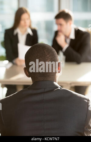 African American männlichen Kandidaten warten auf Personalentscheidung auf Vorstellungsgespräch, kaukasische Arbeitgeber lesen Zusammenfassung auf Hintergrund. tausendjährigen Schwarz m Stockfoto