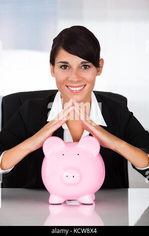 Junge glücklich Geschäftsfrau Holding rosa Sparschwein am Schreibtisch Stockfoto