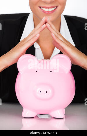 Junge glücklich Geschäftsfrau Holding rosa Sparschwein am Schreibtisch Stockfoto