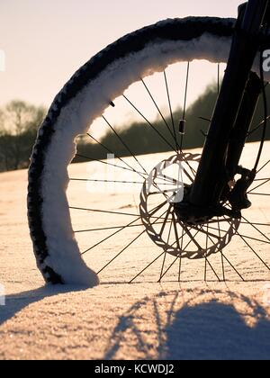 Das Vorderrad der Mountainbike Aufenthalt im Pulverschnee. verloren Pfad unter tiefe Schneeverwehungen. Schneeflocken schmelzen in dunklen off road Reifen. Winter in Th Stockfoto