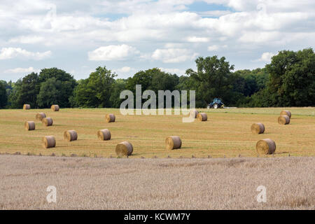 LIMOUSIN, Frankreich - Juli 5, 2017: Ackerland mit Weizenfeldern im Vordergrund und einem Traktor, der das Land unter geerntetes Heu arbeiten in der Ba Stockfoto