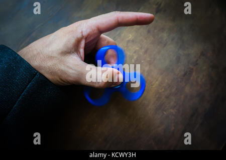 Ein Mann hand Halten einer Hand Spinner oder zappeln Spinner auf dem Hintergrund der hölzernen Tisch. Leistungsstarke Spinner, Twister für Hände Unterhaltung rotierende Spielzeug. Stockfoto