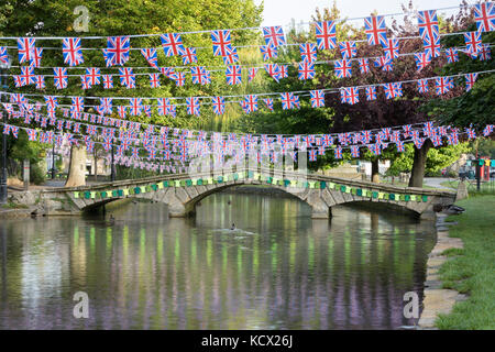 Steinerne Brücke über den Fluss Windrush mit gestrickten Radfahren Westen und Union Jack Flags für die Tour von Großbritannien Radrennen eingerichtet Stockfoto