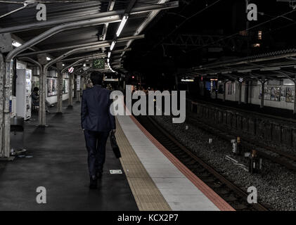Ein japanischer Angestellter, der mitten in der Nacht von der Arbeit nach Hause zurückkehrt. Sie können die Uhrzeit auf der Senderuhr sehen. Stockfoto
