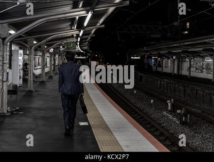Eine Japanische Salaryman auf dem Heimweg von der Arbeit mitten in der Nacht. kann man die Zeit auf der Station. Stockfoto
