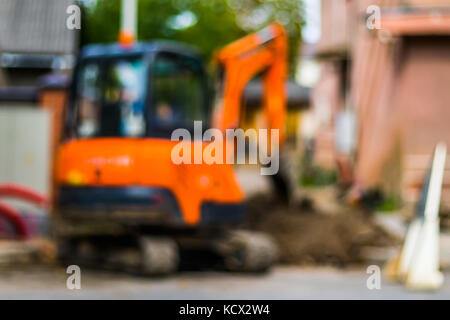 Abstrakte verschwommenen Hintergrund - kleine Bagger mit Mann nach Innen, in der Arbeit, die Straße zu reparieren. Stockfoto