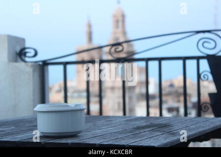 Weiß Aschenbecher auf Holztisch im Fokus, mit unscharfen Stadt im Hintergrund. Stockfoto