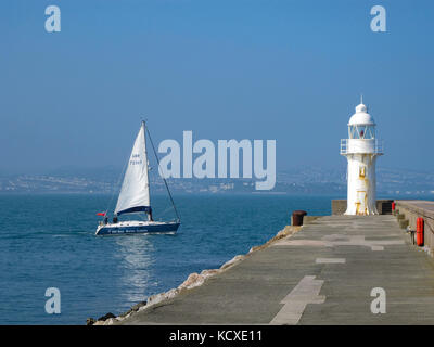Segelboot, Yacht vorbei am Leuchtturm am Ende der Mole in Brixham, Torbay, die Englische Riviera, Devon, Großbritannien. Sommer. Kopieren Sie Platz. Meeresfrüchte Küste Stockfoto