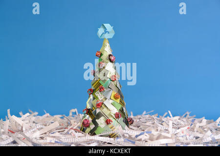 Ökologische Weihnachtsbaum aus Zeitungsausschnitten mit Papierkorb 3-Pfeil auf der Oberseite über blauer Hintergrund Stockfoto