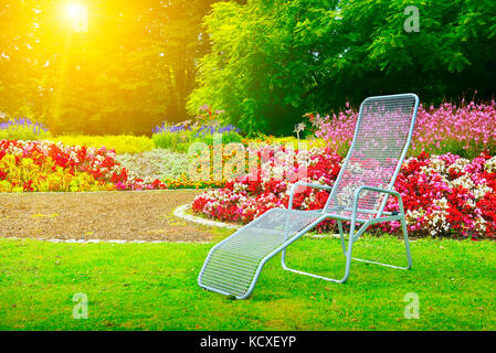 Liegestuhl im Park neben Blumenbeet in der Morgendämmerung Stockfoto