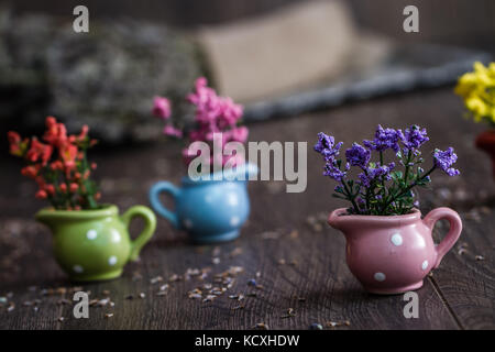 Künstliche kleine gelbe, violette und rote Blumen in kleinen Blumentöpfen auf hölzernen Hintergrund Stockfoto