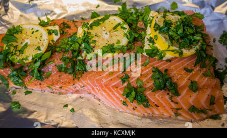 Eine nahrhafte Stück roh rosa Lachs, mit in Scheiben geschnittenen Zitrone Stücke auf der Oberseite, garniert mit Petersilie, bereit, im Ofen gebacken werden. Stockfoto