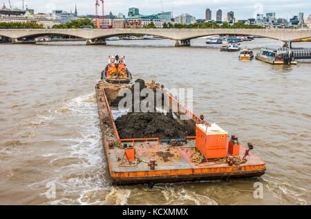 Ein Schlepper Ziehen eines beladenen Lastkahn, Richtung Waterloo Bridge über die Themse, mit anderen Schiffen in der Nähe, in London, England, UK. Stockfoto