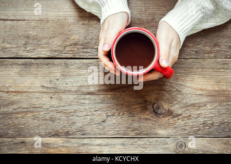 Weibliche Hände halten roten Tasse heiße Schokolade (Kaffee) auf rustikalen Holzmöbeln Hintergrund mit Kopie Raum Stockfoto