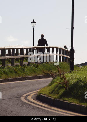 Menschen flanieren über den Aufstieg von einem Hügel Silhouette durch eine hohe Sonne auf den Nordosten coastlin.. Stockfoto