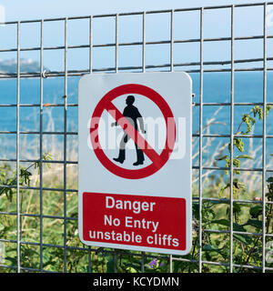 Schwarz, Rot und Weiß Warnschild - kein Eintrag instabil Klippen - ein Zaun auf dem South West Coast Path in der Nähe von Paignton, Torbay Stockfoto