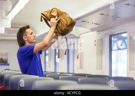 Junger Mann Gepäck auf dem obersten Regal in Flugzeugen Stockfoto