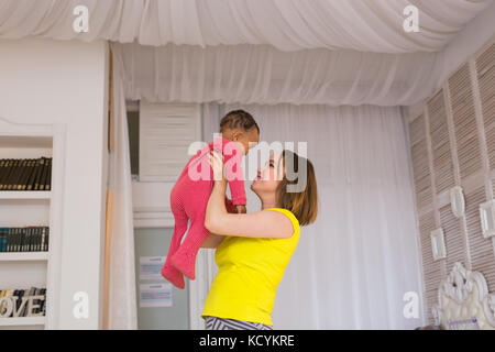 Glückliche Familie. Mutter wirft durcheinander Rennen Baby, zu Hause spielen Stockfoto