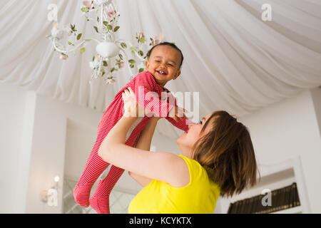 Glückliche Familie. Mutter wirft durcheinander Rennen Baby, zu Hause spielen Stockfoto