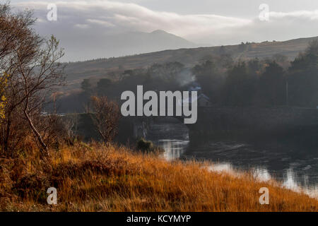 Herbst im County Donegal, Rauch aus einem Schornstein hinter einer alten Steinbrücke über den Fluss Lackagh, Irland steigt. . Stockfoto