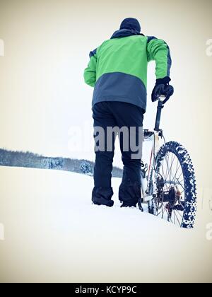 Mann mit Mountainbike Aufenthalt im Pulverschnee. verloren weg in tiefe Schneeverwehungen. Hinterrad detail. Schneeflocken schmelzen in dunklen off road Reifen. Winter Wetter können Sie Stockfoto