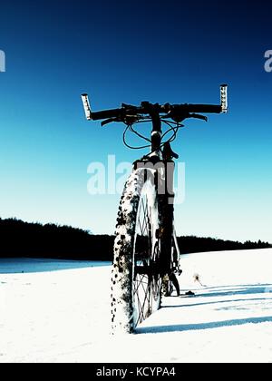 Extremme Kontrast. Mountainbike Aufenthalt im Pulverschnee. verloren weg in tiefe Schneeverwehungen. Hinterrad detail. Schneeflocken schmelzen in dunklen off road Reifen.Win Stockfoto