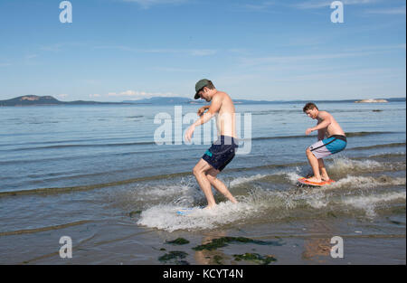 Junge Männer skim Boarding am Strand von Sidney Island, British Columbia, Kanada Stockfoto