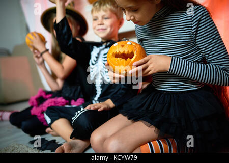 Closeup Portrait von drei Kindern tragen Halloween Kostüme sitzen auf dem Boden im Zimmer, auf Mädchen mit kleinen geschnitzten Kürbis Fokus Stockfoto