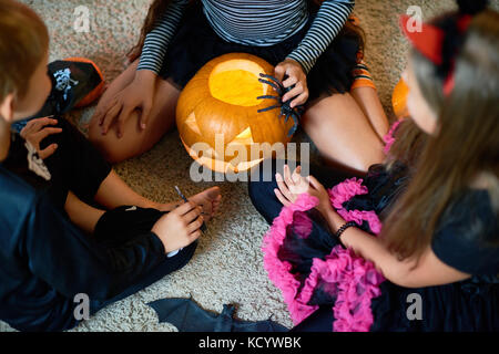 Oben Ansicht von drei Kindern tragen Halloween Kostüme spielen magic Ritual mit Kürbis Laterne sitzen auf dem Boden im Kreis Stockfoto