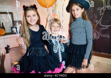 Portrait von drei glückliche Kinder tragen Kostüme mit Ballons in eingerichtete Zimmer Halloween feiern Posing Stockfoto