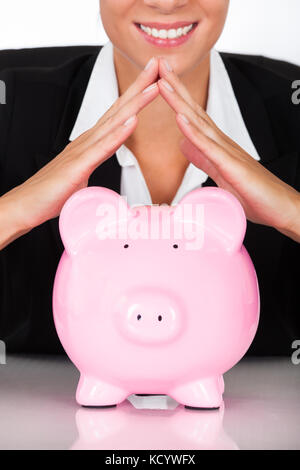 Junge glücklich Geschäftsfrau Holding rosa Sparschwein am Schreibtisch Stockfoto
