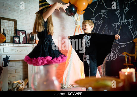 Fröhliche Kinder tragen Halloween Kostüme holding Generalprobe vor der Teilnahme an Trick-or-Treaten, Interieur der Zimmer auf Hintergrund Stockfoto