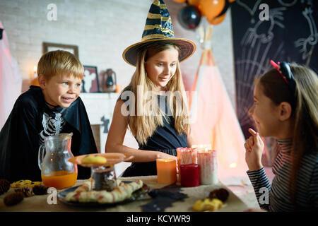 Profil anzeigen von hübsches Mädchen erzählte Gruselgeschichte erzählt, um ihre kleinen Freunde während Halloween zu Hause feiern, Tisch für Urlaub Abendessen am Vordergrund Stockfoto